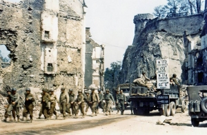 United States Army trucks and jeeps drive through the ruins of Saint-Lô